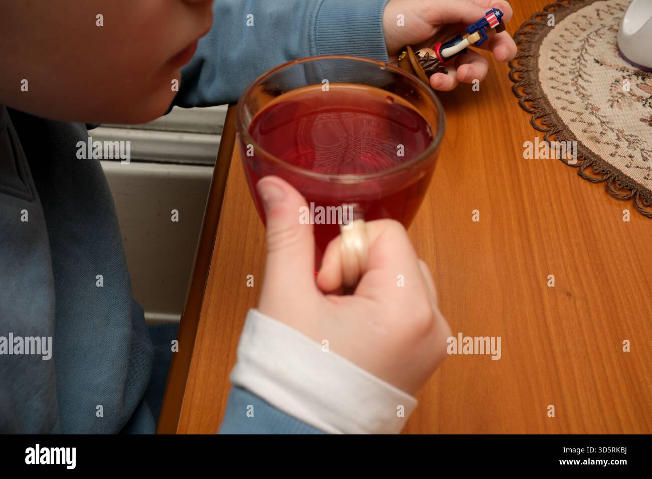 Ein Kind sitzt an einem Holztisch und genießt an einem kühlen Tag eine warme Tasse hellen Tee. Stockfoto