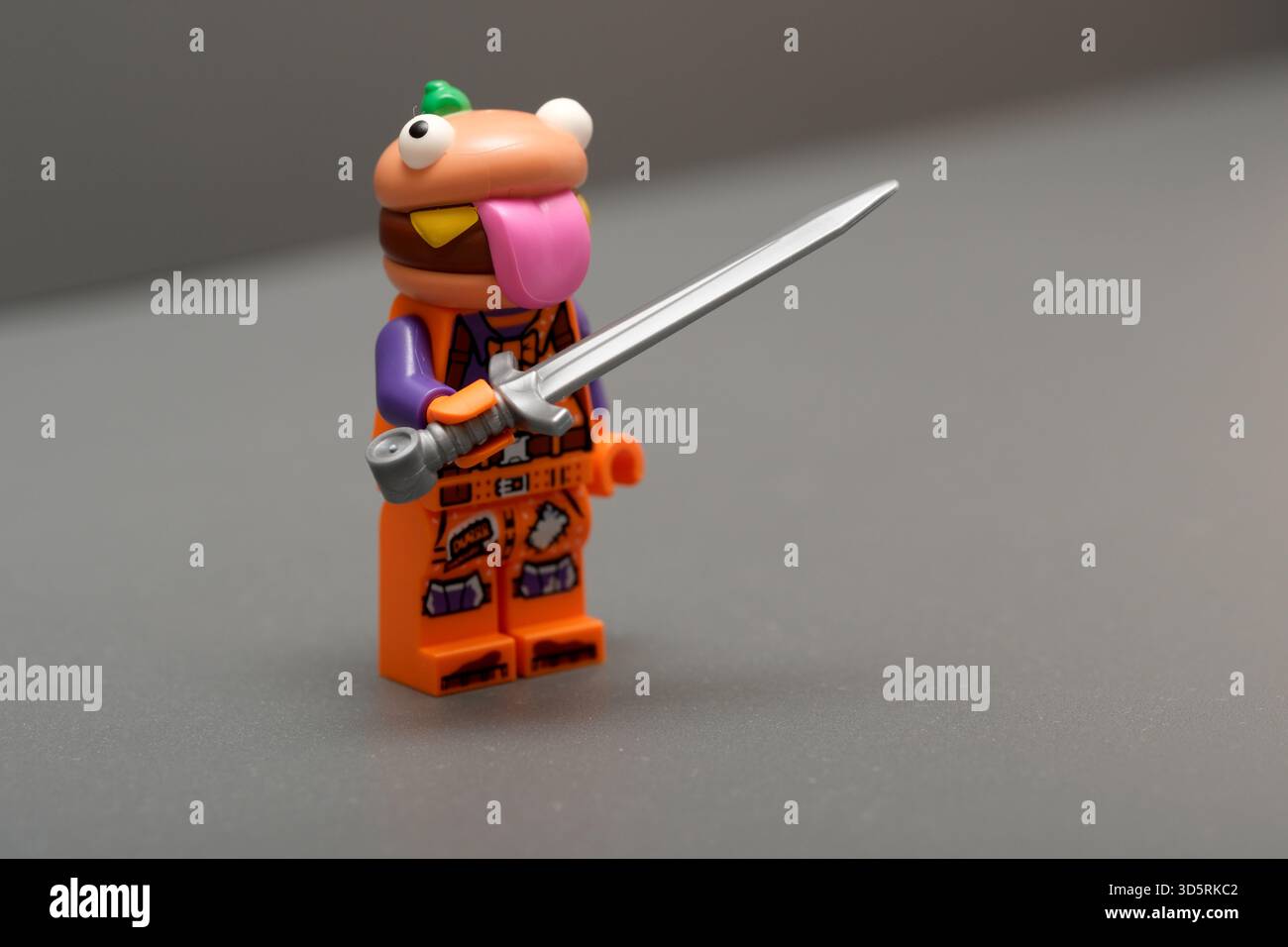 Ein verspielter Charakter mit einem lustigen Gesicht hält ein glänzendes Schwert und zeigt seinen tapferen Geist. Stockfoto