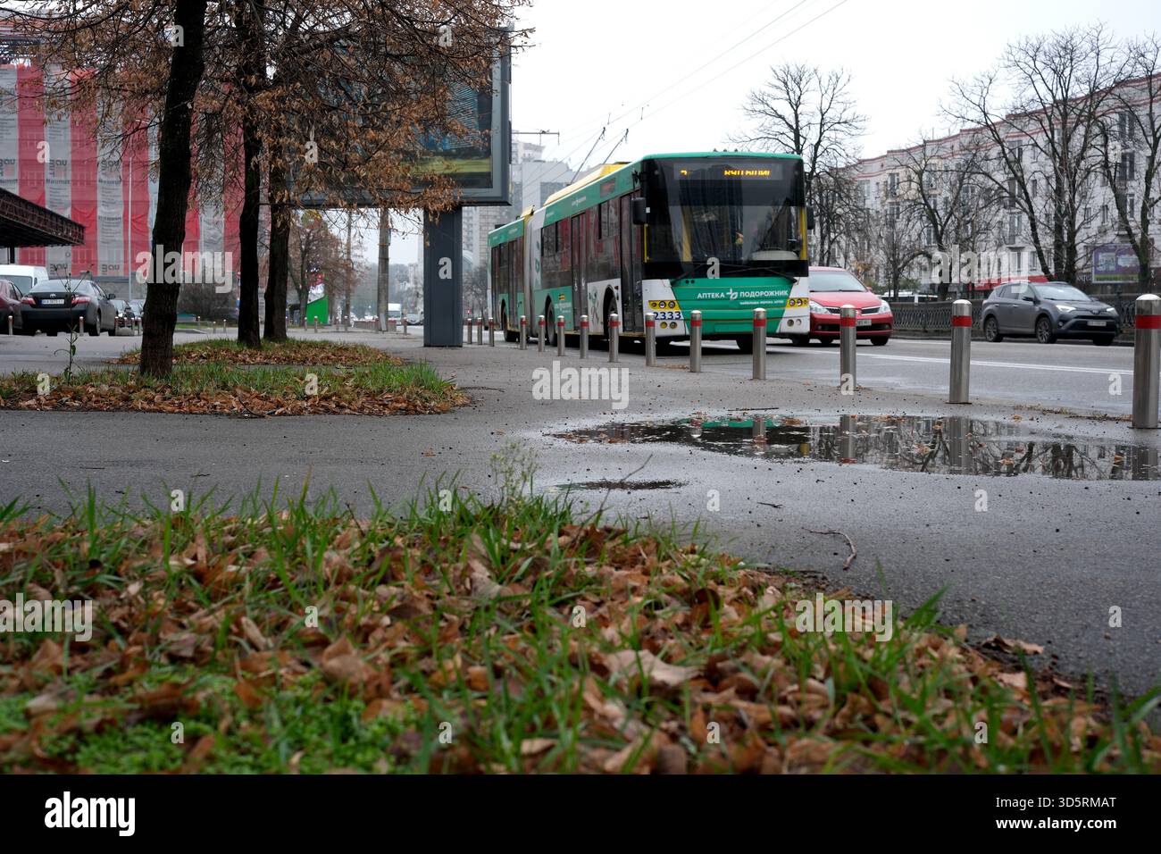 Blätter verstreut auf dem Boden, während ein Bus entlang einer befahrenen Straße in Kiew fährt. Stockfoto