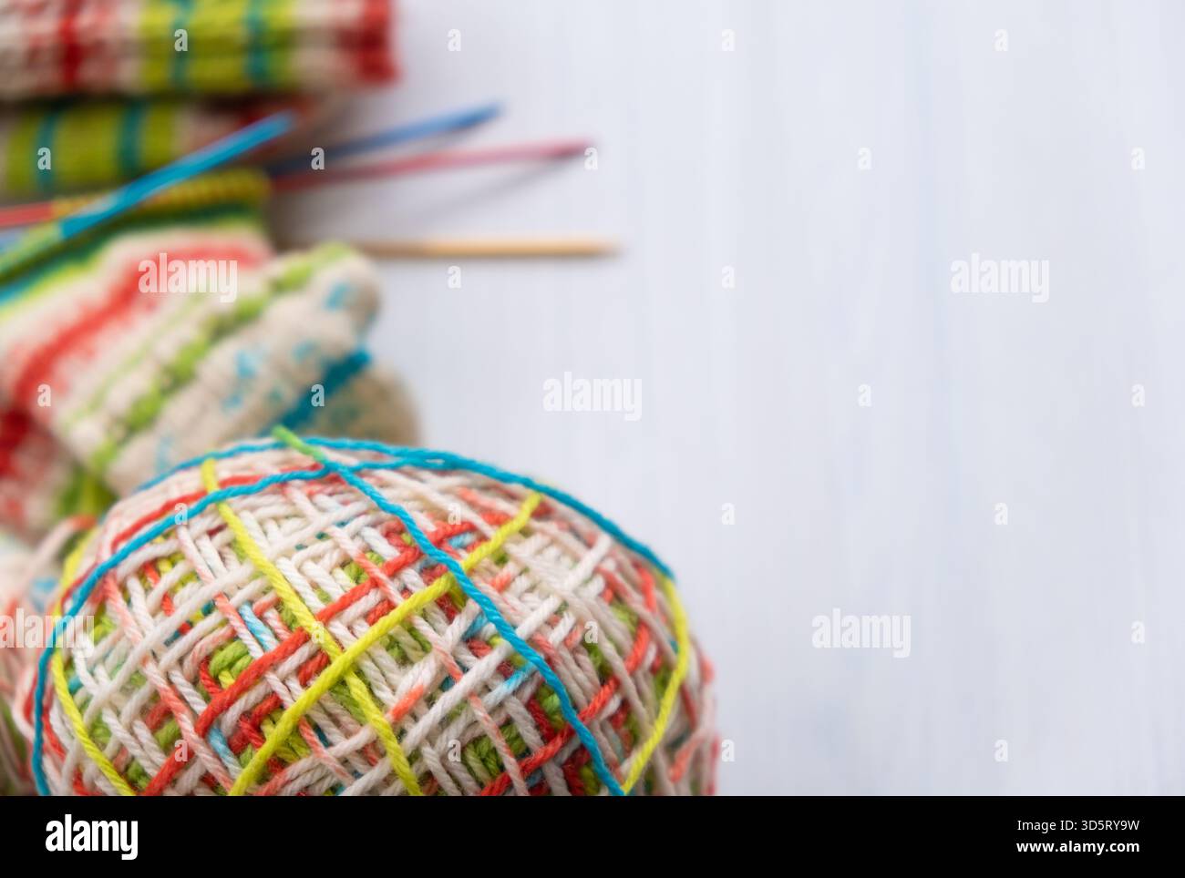 Farbenfrohes Wollgarn neben Stricksocken mit klarem Kopierraum, mit leuchtenden Fasern und weichen Texturen, ideal zum Basteln von Motiven, Produktdetails Stockfoto
