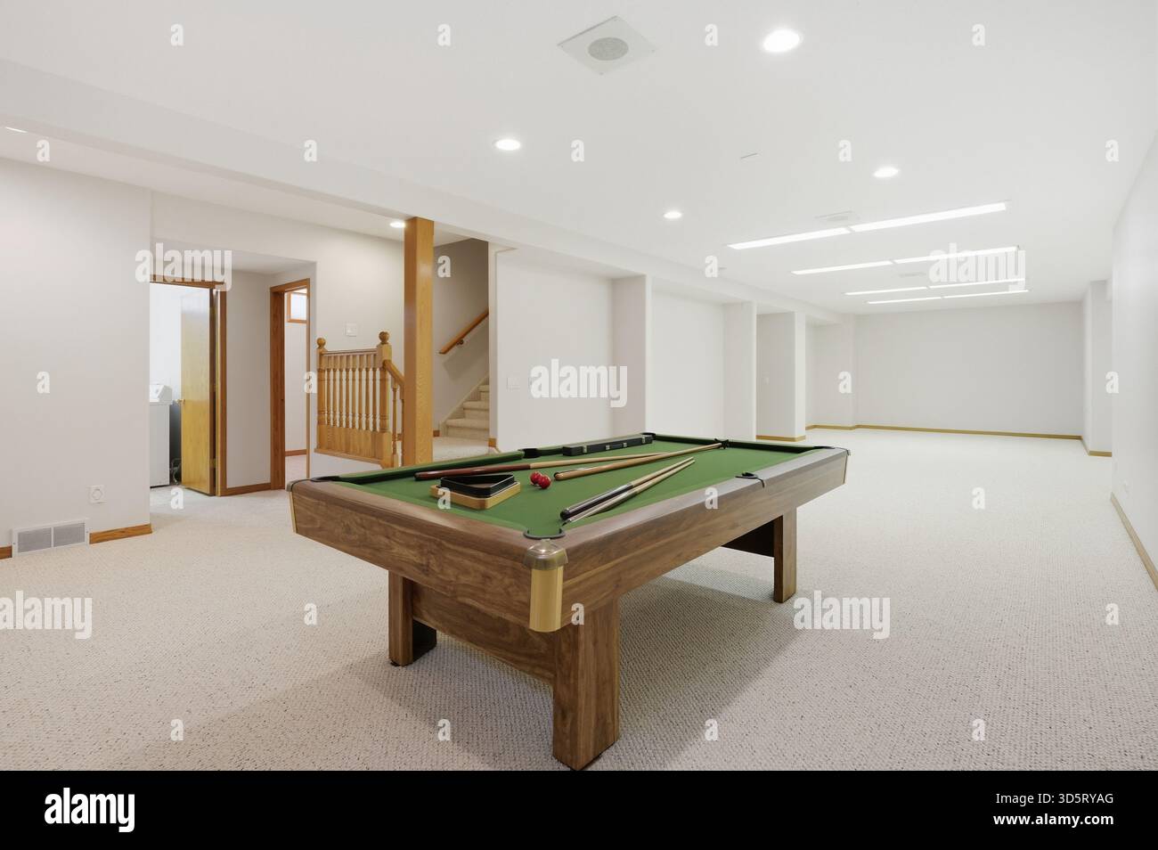 Billardtisch steht in einem großen, leeren Raum. Das Zimmer ist größtenteils weiß mit ein paar braunen Akzenten. Der Billardtisch ist von einem Teppichboden umgeben Stockfoto