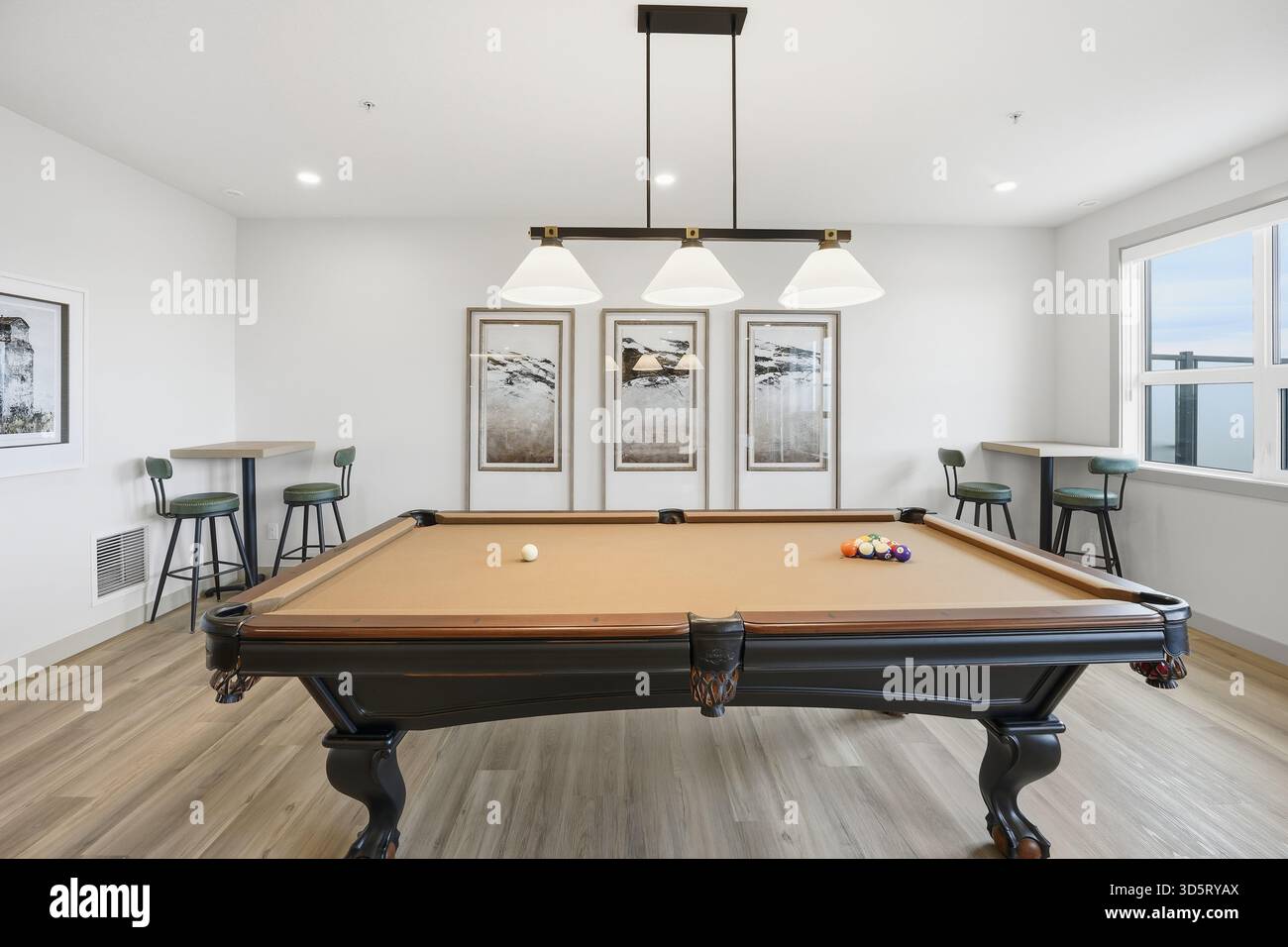 Der Billardtisch ist von Stühlen und einem Fenster umgeben. Das Zimmer ist schwach beleuchtet und hat eine gemütliche Atmosphäre Stockfoto