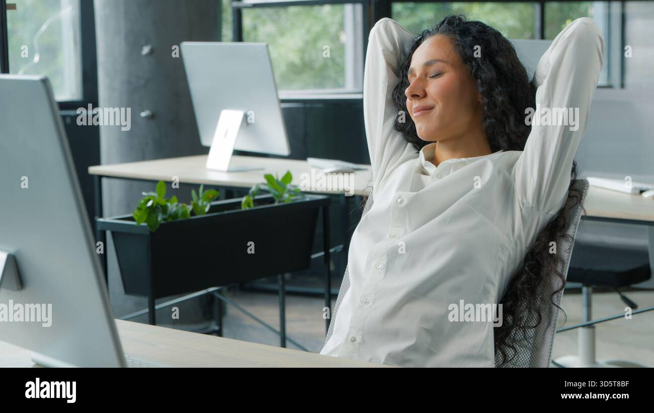 Entspannende friedliche hispanische Geschäftsfrau macht Pause im Büro Geschäftsfrau ruht Hände hinter Kopf und erledigt die Arbeit in Stockfoto