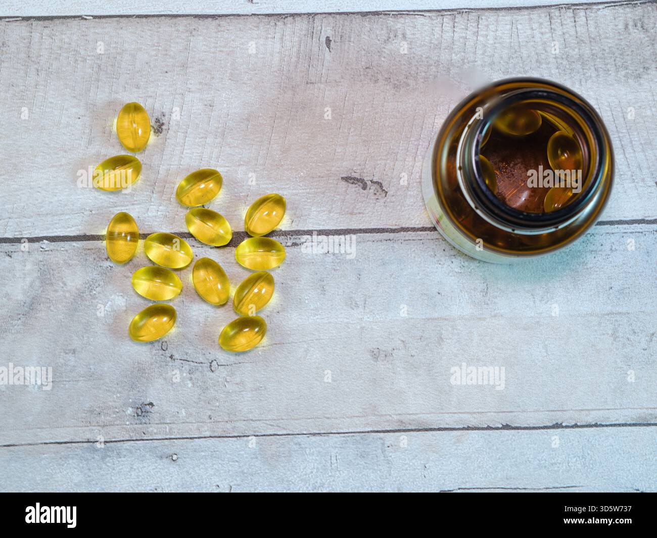 Gelbe Omega-3-Fischöl-Kapseln - gelbe Omega-3-Softgel-Kapseln, die aus einer bernsteinfarbenen Flasche auf einem hellen Holzhintergrund verschüttet werden. Perfekt für die Gesundheit, nu Stockfoto