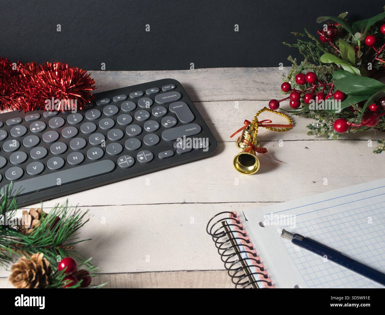 Festlicher Arbeitsbereich mit Tastatur – Eine moderne, dunkle Tastatur, umgeben von festlichem rotem Lametta, goldenen Glocken und grünen Kiefernzweigen in rustikalem Ambiente Stockfoto