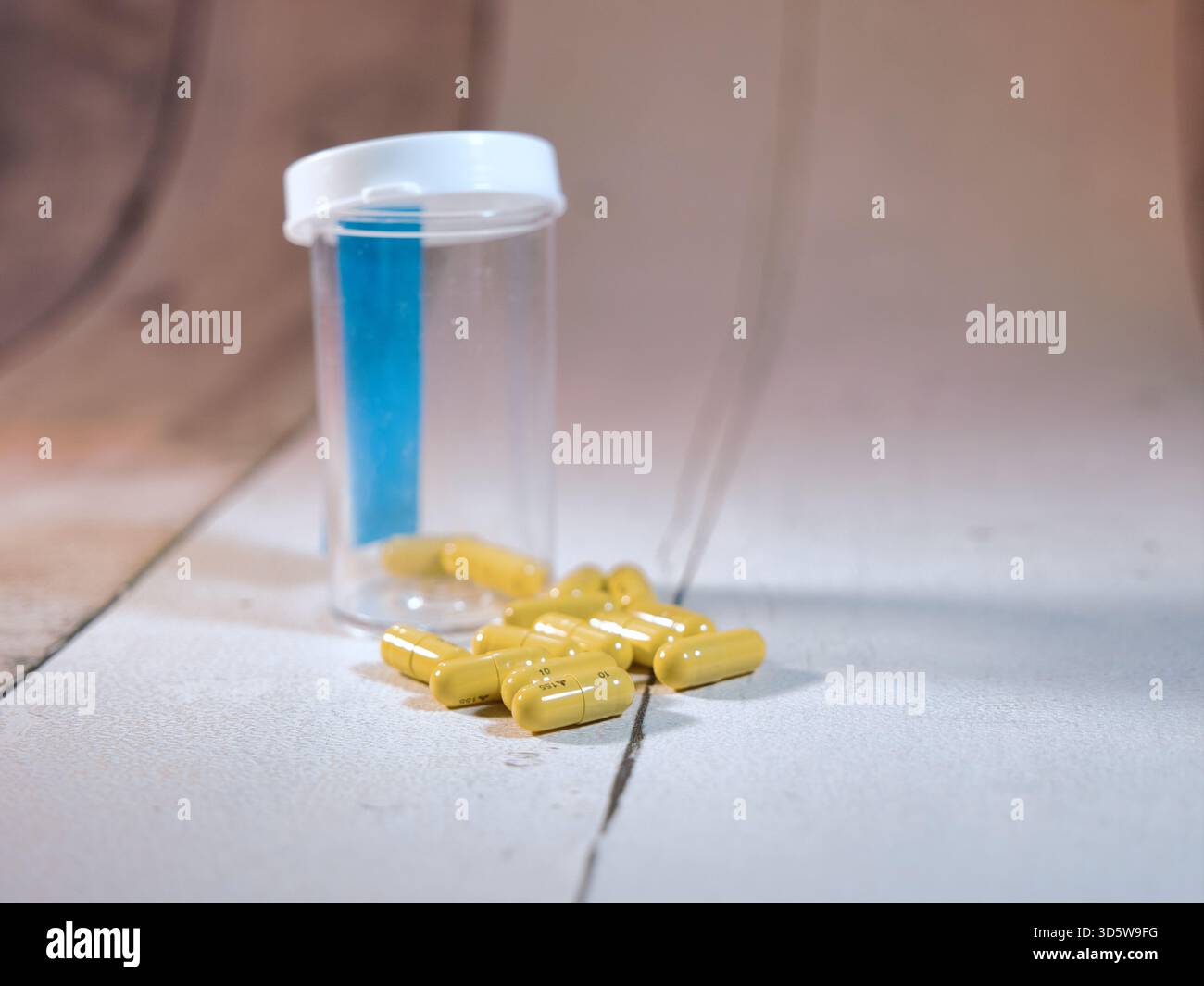 Verschüttete gelbe Kapseln, Pille Flasche - Nahaufnahme von gelben Kapselpillen, die aus einer leeren verschreibungspflichtigen Flasche auf einer strukturierten weißen Oberfläche verschüttet wurden, Symboli Stockfoto