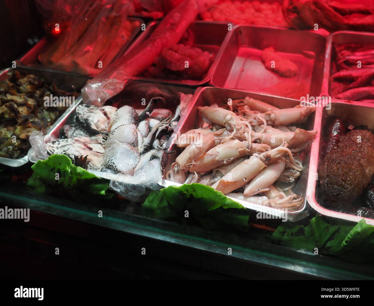 Taipeh, Taiwan - 17. November 2024: Eine Vitrine auf einem Nachtmarkt mit Metallschalen mit Rohstoffen, darunter Tintenfisch und gehäutete Frösche. Stockfoto
