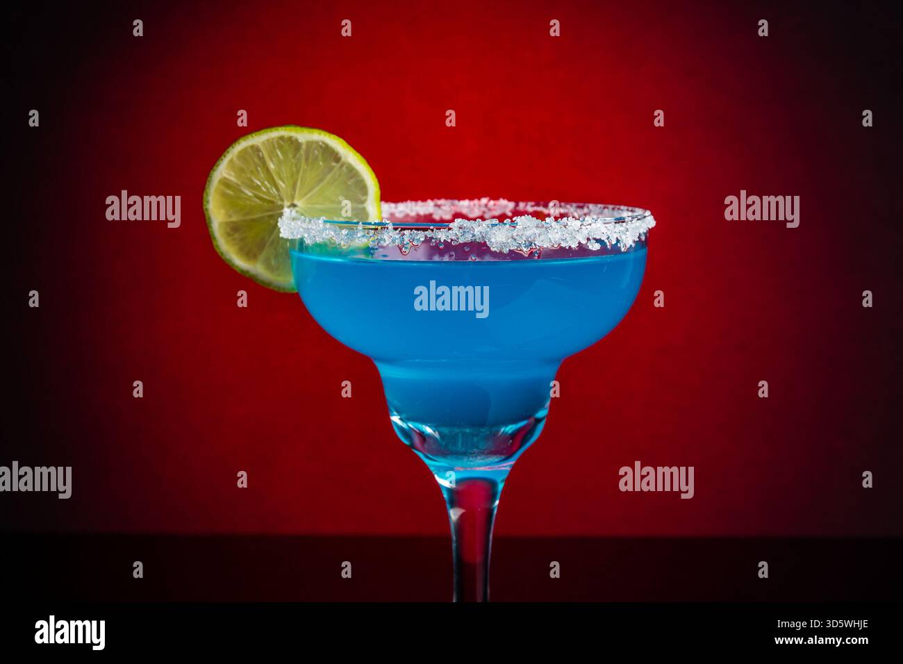 Ein blauer Cocktail in einem Margarita-Glas mit gesalzenem Rand und Limettenscheibe, reflektiert auf schwarzer Oberfläche. Stockfoto