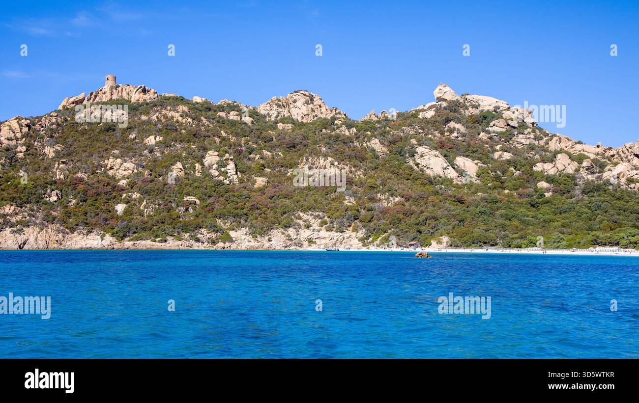 Die Bucht von Roccapina mit ihrem wunderschönen türkisfarbenen Wasser vom Meer aus gesehen, mit dem Wachturm und liegendem Löwen auf dem Hügel in der Sonne Stockfoto