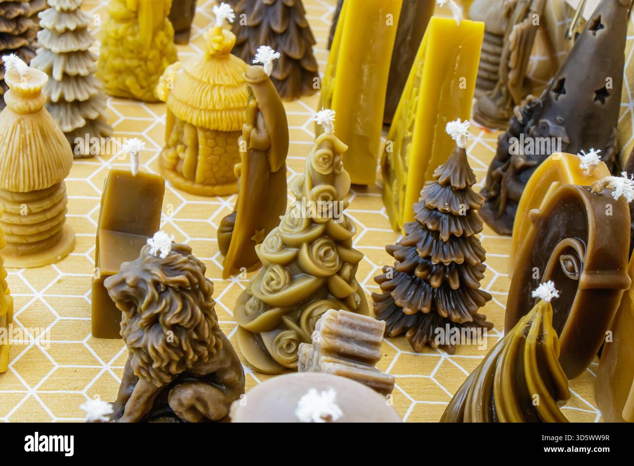 Eine Auswahl handgefertigter Kerzen in verschiedenen Formen – wie Bäume und Tiere – ist ordentlich auf einer gelben Oberfläche angeordnet und unterstreicht ihre komplexen Designs Stockfoto