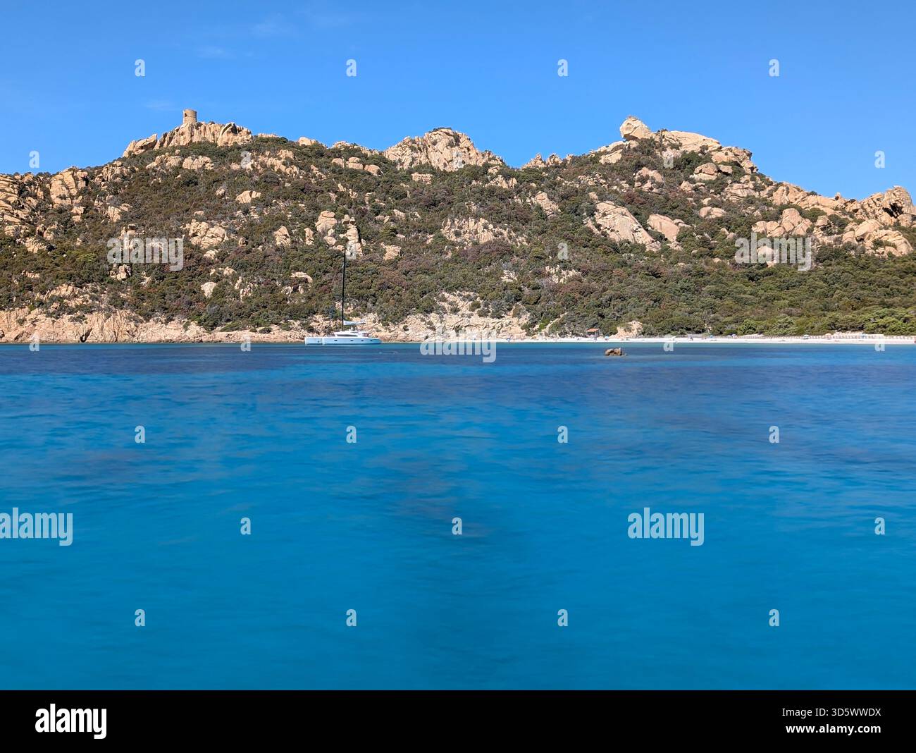 Die Bucht von Roccapina mit ihrem wunderschönen türkisfarbenen Wasser vom Meer aus gesehen, mit dem Wachturm und liegendem Löwen auf dem Hügel in der Sonne Stockfoto