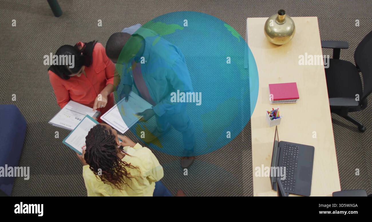 Das Pointing-Team lehnt sich über die Dozenten an den niedrigen Tisch des Büros, Korallenplatte, blaue Jacke, gelbe Spitze, Globus Stockfoto