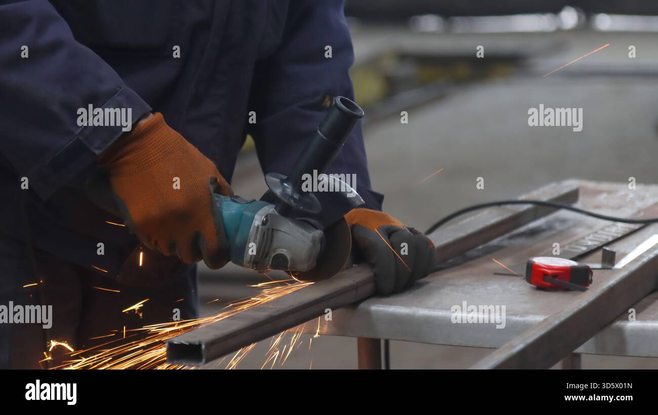 Industrielles Schneiden von Metall durch einen Arbeiter mit einem Halos von hellen Funken aus einem Winkelschleifer Stockfoto