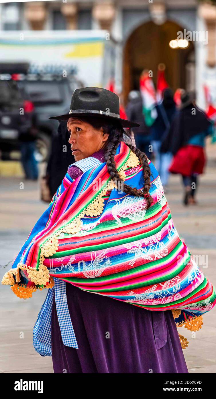 Bolivianische Frau in traditioneller Andenkleidung mit farbenfrohem Manta und geflochtenem Haar, die in einer städtischen Straße in Bolivien spaziert. Stockfoto