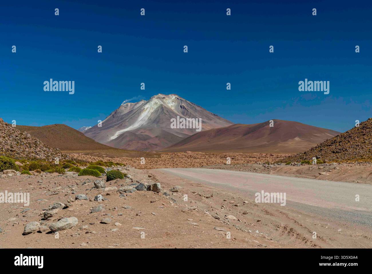 Wüstenstraße, die in Richtung eines vulkanischen Berges in einer abgelegenen Höhenlandschaft unter einem klaren tiefblauen Himmel führt – Andenaltiplano, Bolivien Stockfoto