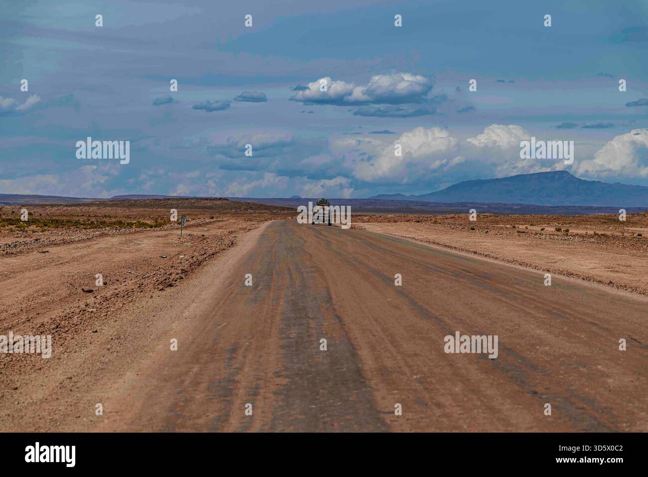 Unbefestigte Straße durch die trockene Landschaft des Andenaltiplano unter einem dramatischen Himmel, mit Bergen und karger Wüstenvegetation – Südamerika Stockfoto