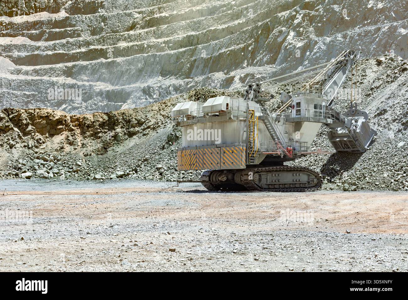 Eine massive elektrische Schaufel gräbt Erz aus der Terrassenmauer einer großen Kupfermine in Chile und zeigt den Umfang des Vorhabens. Stockfoto