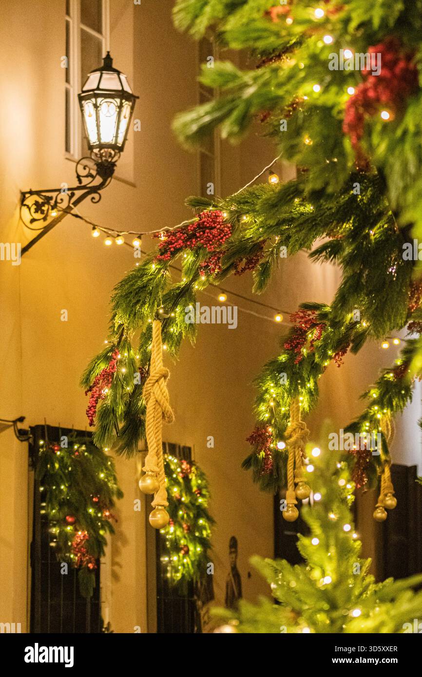 Festliche Weihnachtsdekoration im Freien mit leuchtendem Grün, roten Beeren, hängenden Ornamenten und warmen Lichtern in einer bezaubernden Straße Stockfoto