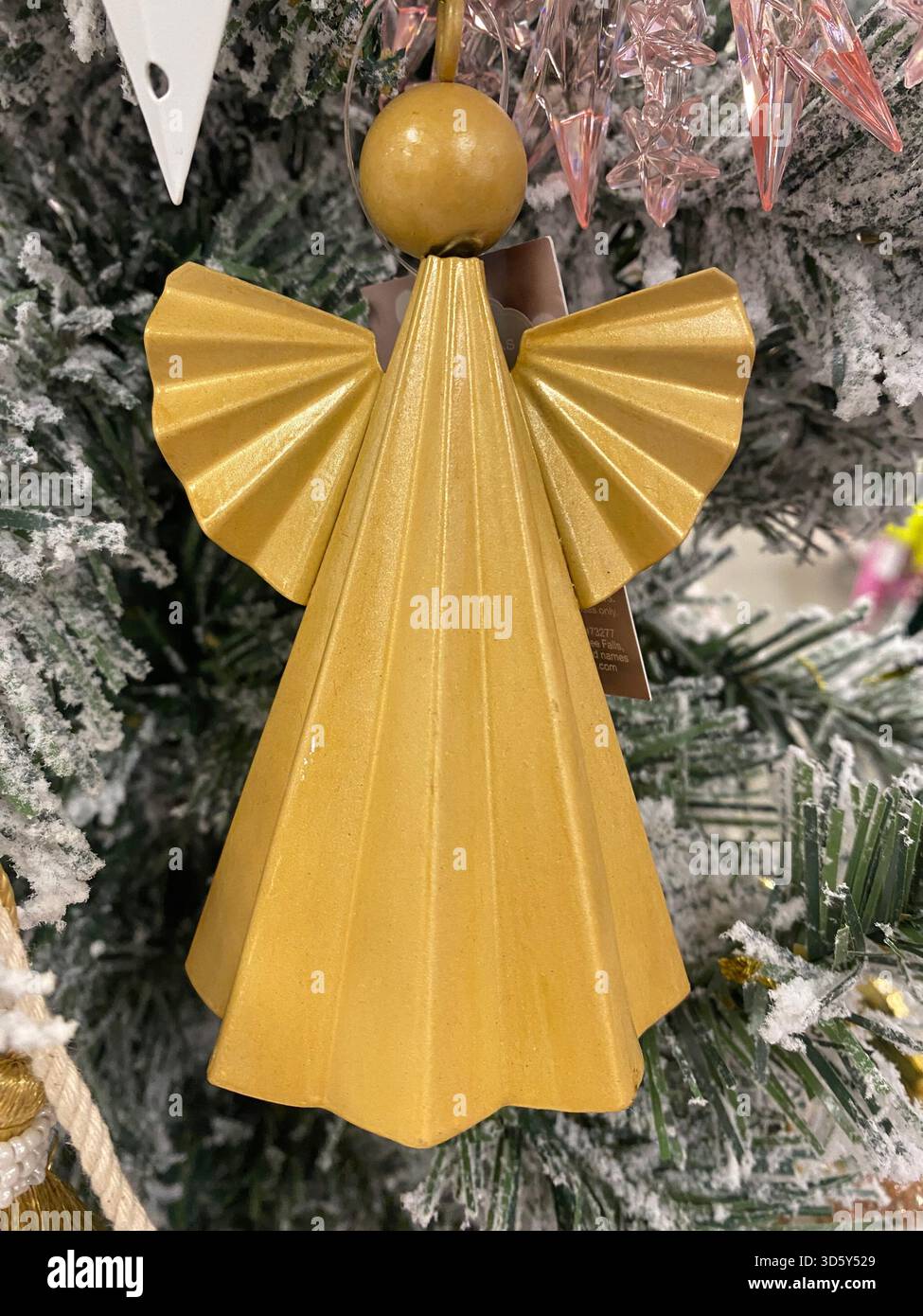 Ein goldener Engelsschmuck mit gefalteten Flügeln, die an einem geschmückten Weihnachtsbaum hängen. Die metallische Oberfläche und die geometrischen Falten sorgen für einen eleganten Look. Stockfoto