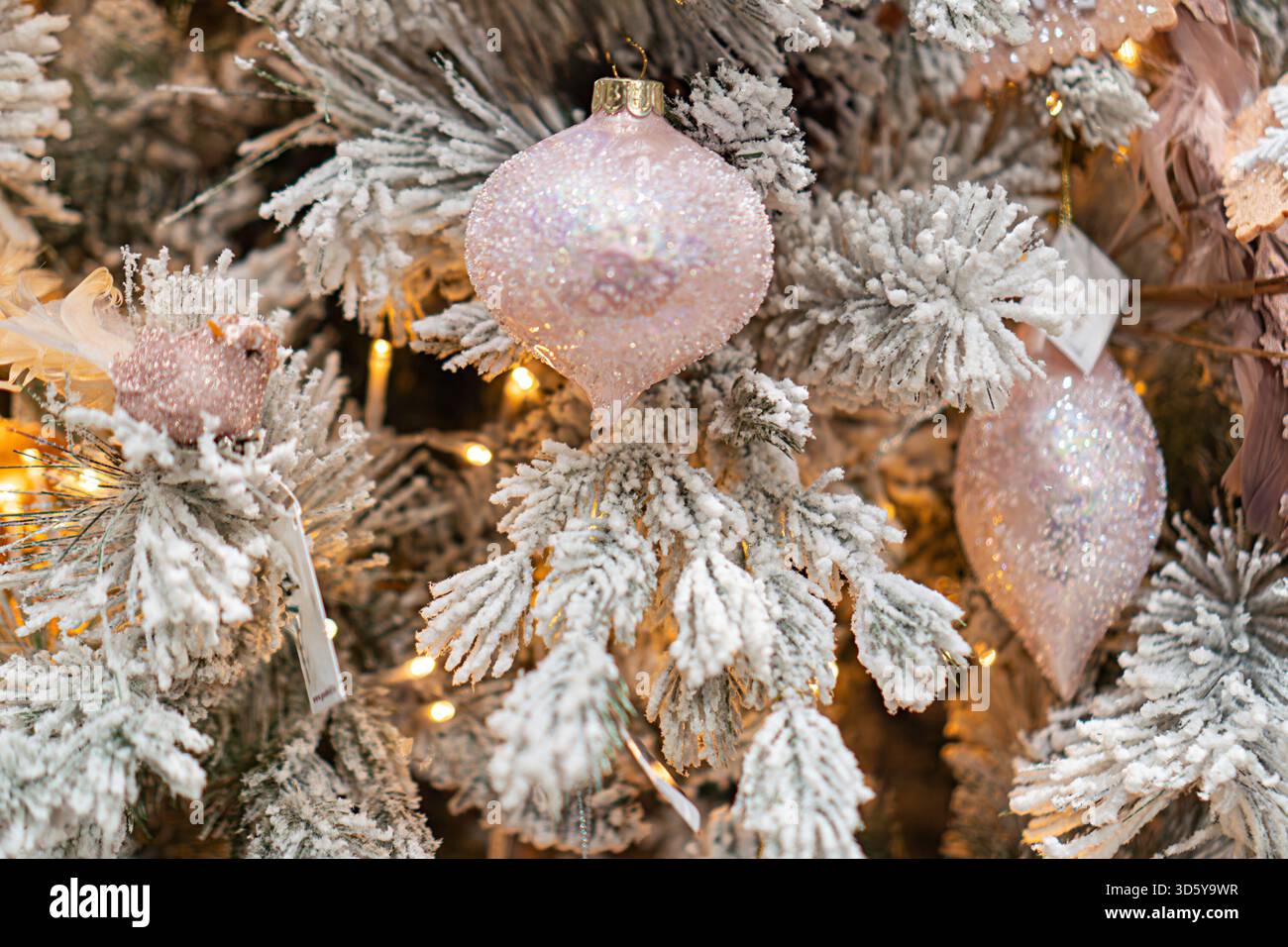 Ein gut dekorierter Weihnachtsbaum, der mit Lichtern und Ornamenten in einer coolen Farbpalette von weiß, Silber und Rosa geschmückt ist. Der Baum hat eine Spitze und ein b Stockfoto
