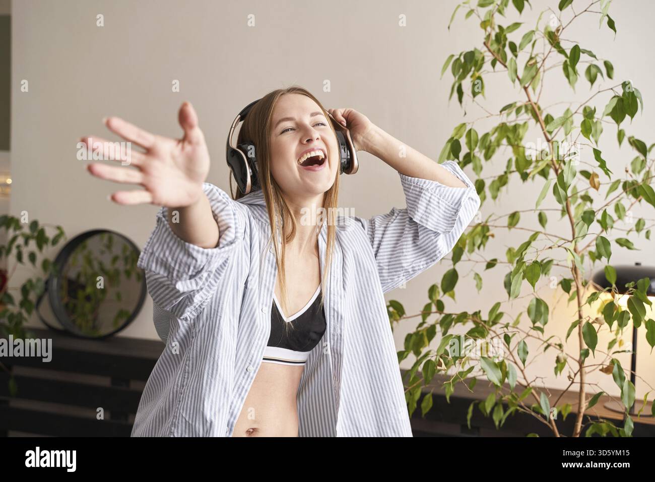 Die junge Frau singt zu Hause. Die Texte des Hauses tanzen. Lustiges Lied. Unabhängiges Frauenporträt. Allein zu Hause. Quarantäneaktion sitzend. Fröhliche Entspannung Stockfoto