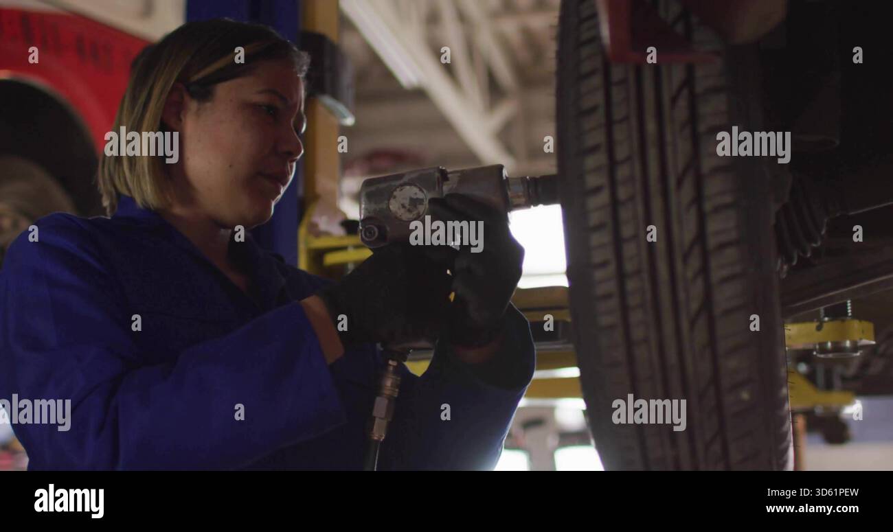 Arbeitsmechaniker in blauen Overalls zum Festziehen der Radmuttern in der Garage mit Schlagschrauber Stockfoto