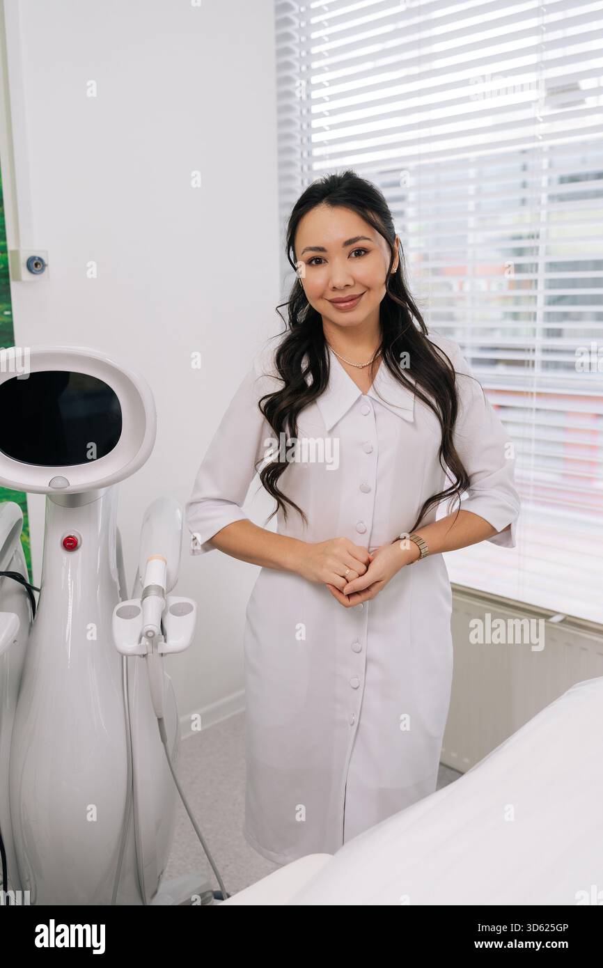 Lächelnde asiatische Kosmetikerin, die in einer modernen Schönheitsklinik steht und fortschrittliche SMAS-Lifting-Technologie für Hautverjüngung und Anti-Aging präsentiert Stockfoto