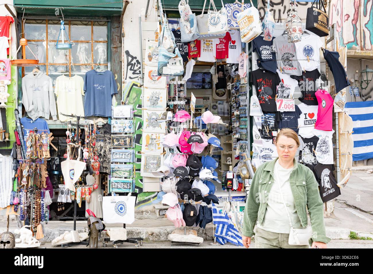 Athen, Griechenland - 15. Mai 2024: Souvenirladen und Frau, die im Touristenviertel vorbeiläuft Stockfoto