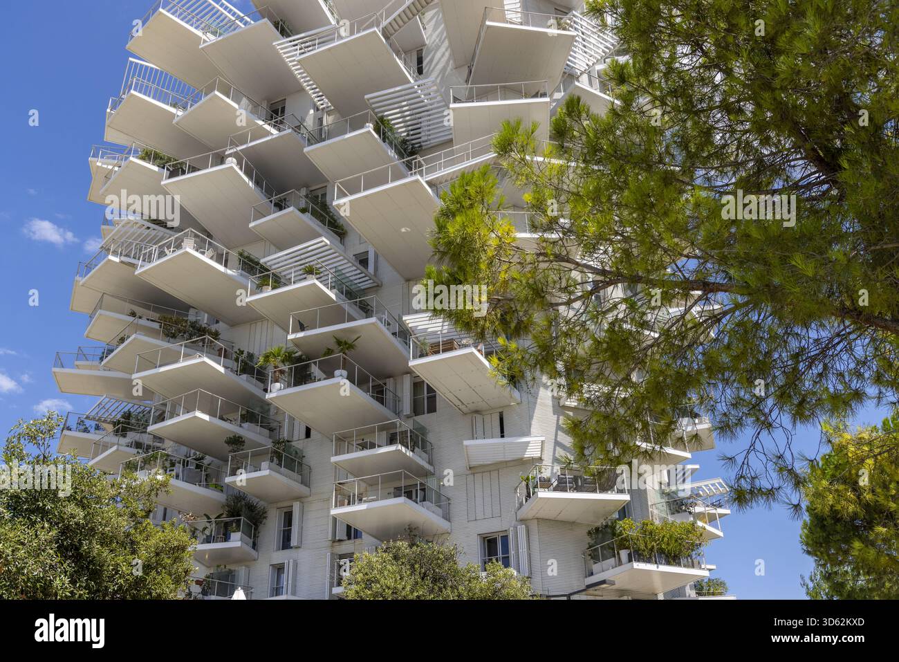 Blick auf ein beeindruckendes modernes Gebäude mit auskragenden Balkonen, die einem Baum ähneln, gegenüber einem klaren blauen Himmel und üppigem Grün, Montpellier, Stockfoto