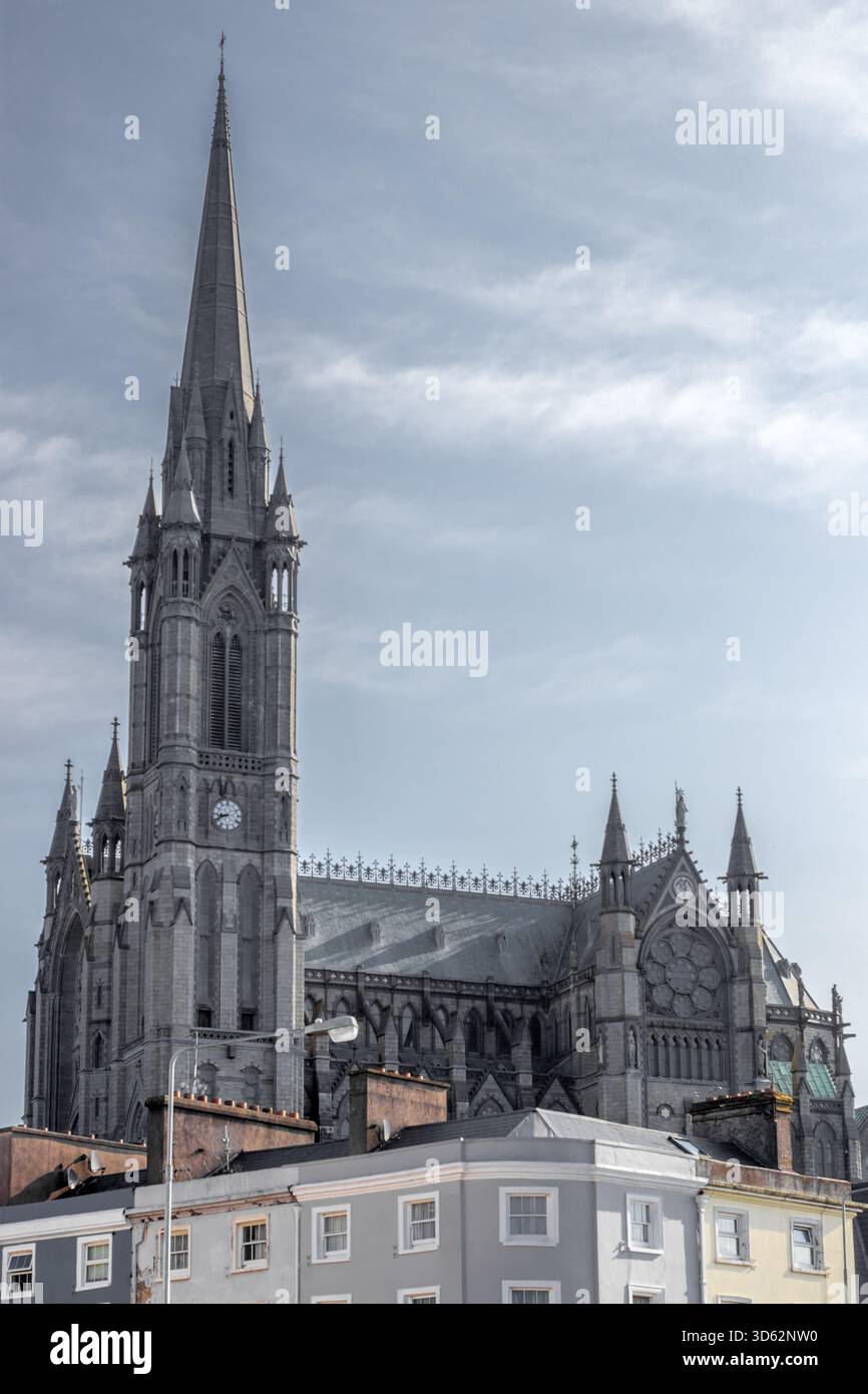 Der Blick auf die St. Colman's Cathedral erhebt sich majestätisch über den bunten Dächern, die gotischen Türme durchdringen den bewölkten Himmel, ein zeitloses Wahrzeichen, Cobh, Graf Stockfoto