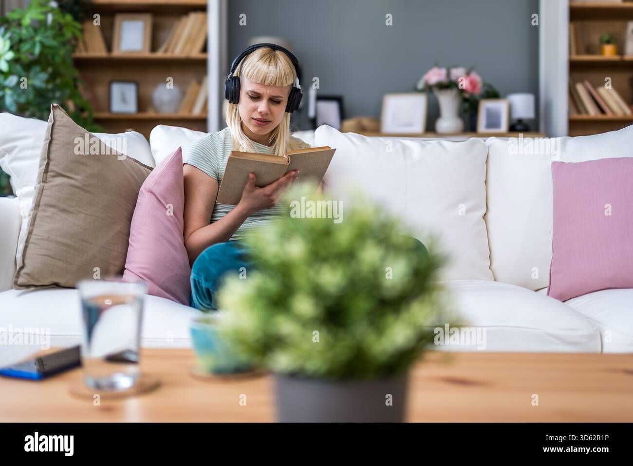 Junge Frau liest ein Buch mit Kopfhörern, mischt leises Studium und Hintergrundmusik; dreht Seiten, kommentiert Passagen, verbessert den Fokus, Vokabular Stockfoto