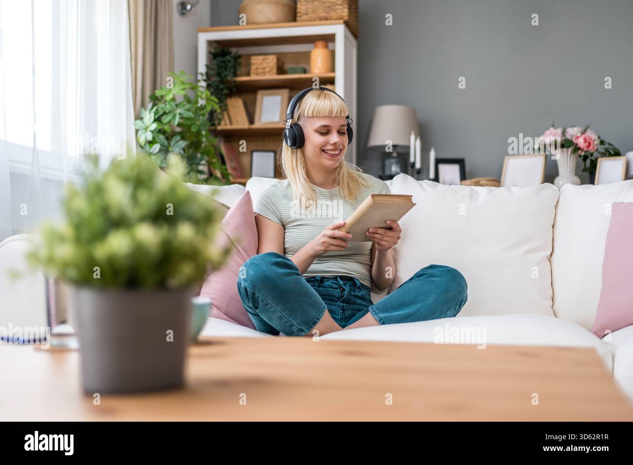 Junge Frau liest ein Buch mit Kopfhörern, mischt leises Studium und Hintergrundmusik; dreht Seiten, kommentiert Passagen, verbessert den Fokus, Vokabular Stockfoto