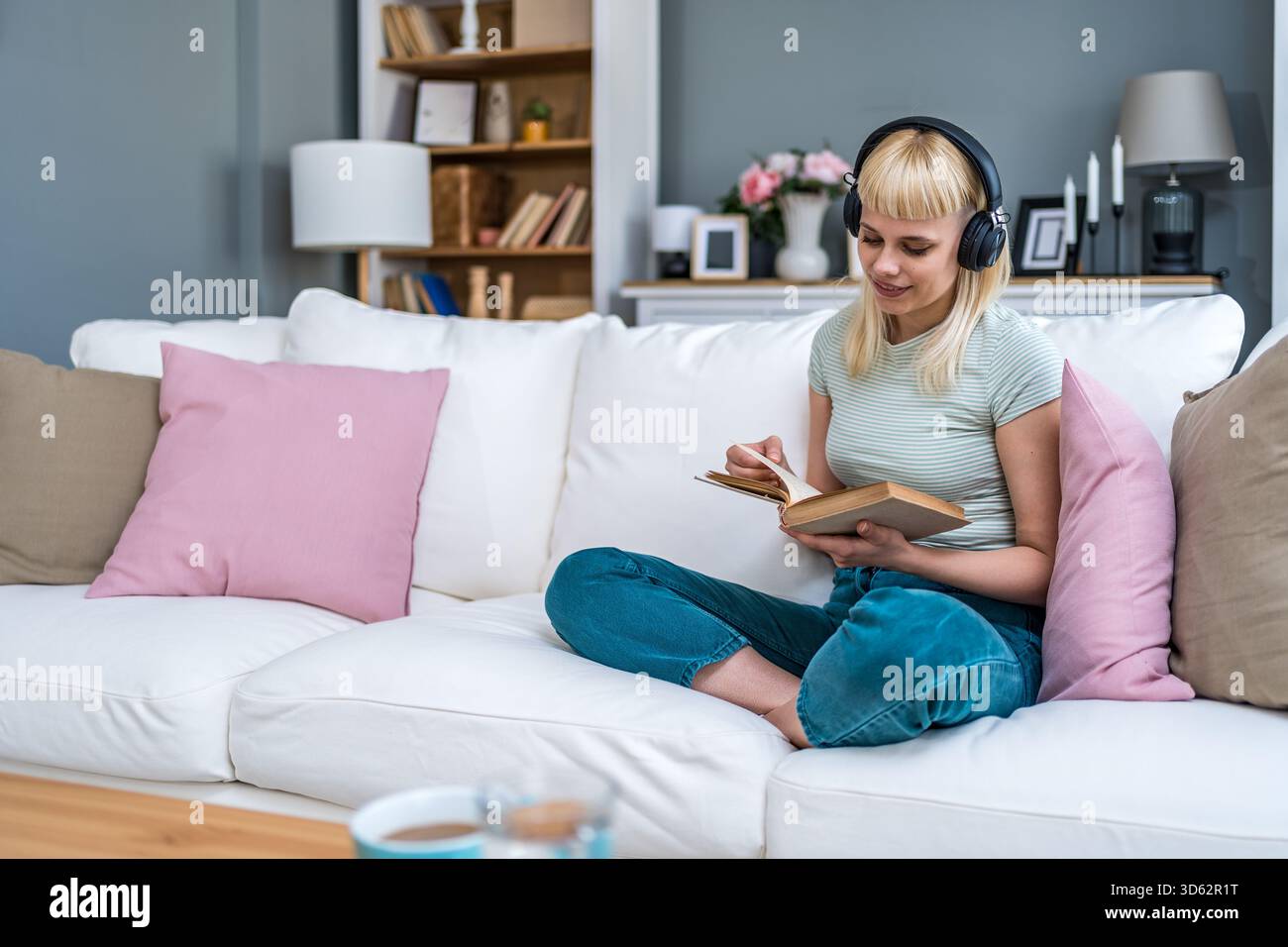 Junge Frau liest ein Buch mit Kopfhörern, mischt leises Studium und Hintergrundmusik; dreht Seiten, kommentiert Passagen, verbessert den Fokus, Vokabular Stockfoto
