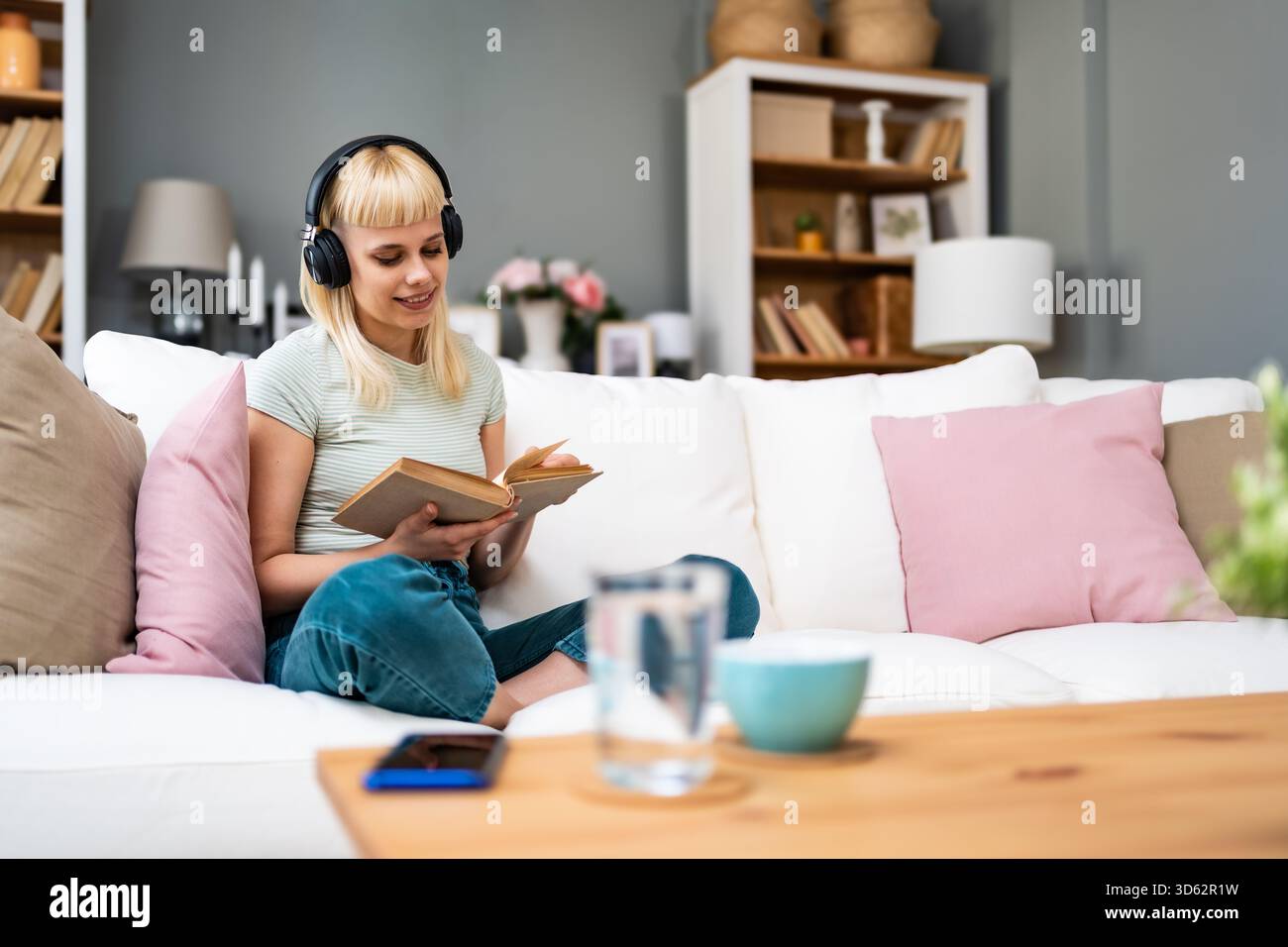 Junge Frau liest ein Buch mit Kopfhörern, mischt leises Studium und Hintergrundmusik; dreht Seiten, kommentiert Passagen, verbessert den Fokus, Vokabular Stockfoto