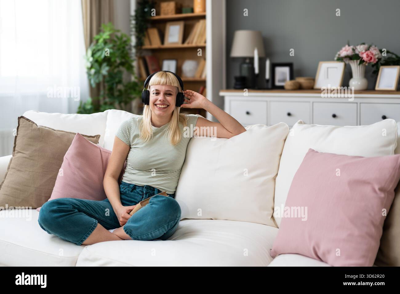 Junge Frau liest ein Buch mit Kopfhörern, mischt leises Studium und Hintergrundmusik; dreht Seiten, kommentiert Passagen, verbessert den Fokus, Vokabular Stockfoto
