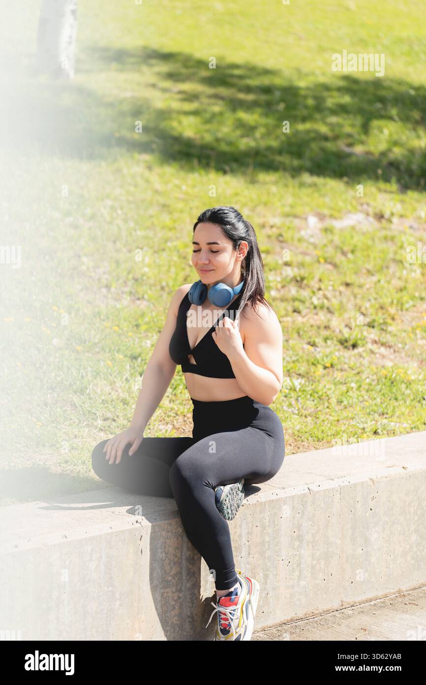 Eine junge Frau ruht sich aus und entspannt sich mit geschlossenen Augen, sitzt im Park, nachdem sie Sport getrieben und Sport getrieben hat Stockfoto