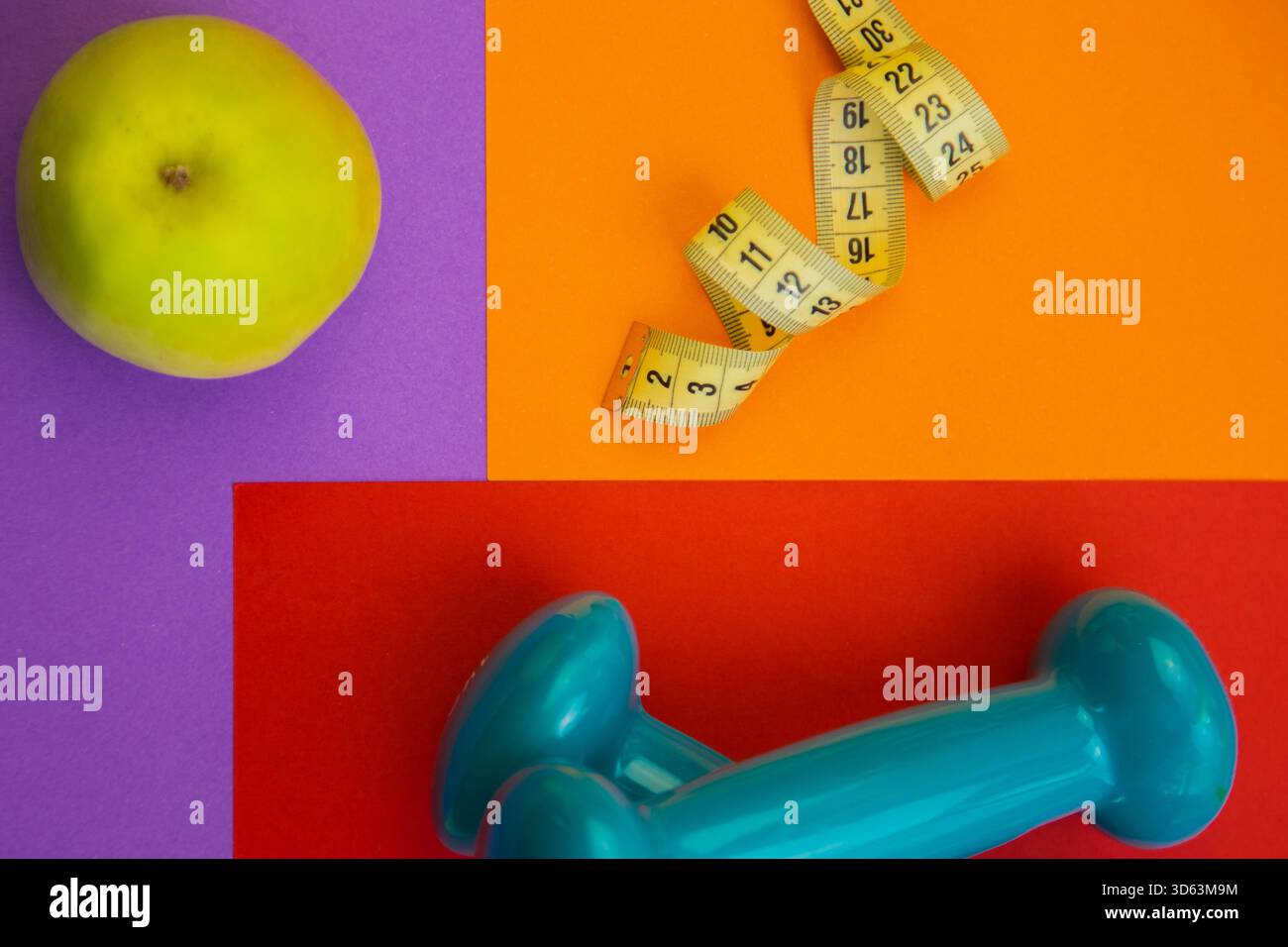 Lebendige Anordnung eines grünen Apfels, Maßband und blaue Hantel auf farbenfroher geometrischer Form Stockfoto
