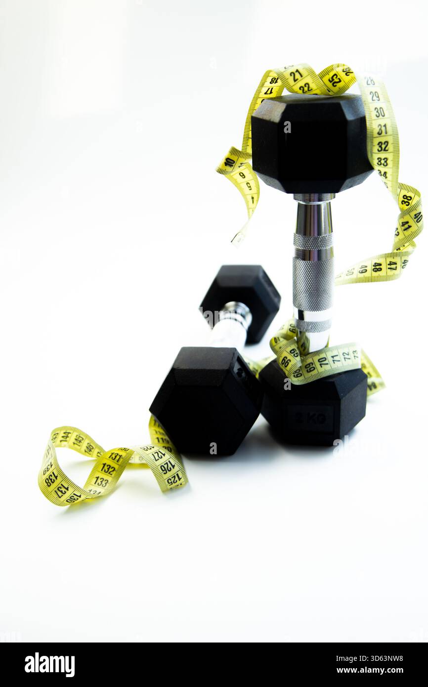 Hanteln sind künstlerisch mit Maßband auf einer sauberen Oberfläche angeordnet, die Fitness und repräsentieren Stockfoto