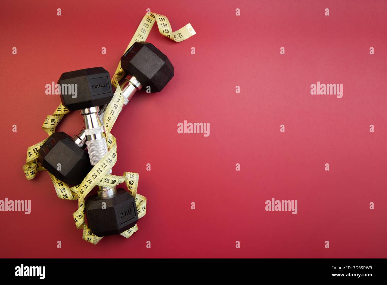 Die Kurzhanteln sind auf einer auffälligen roten Oberfläche positioniert, die mit einem Maßband umwickelt ist, das darstellt Stockfoto