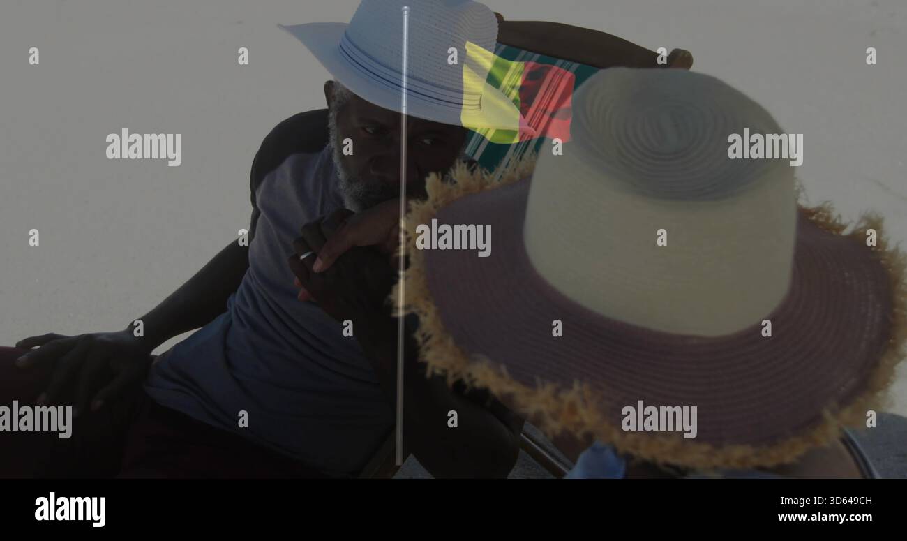 Sprechender Mann in Fedora, der Objekt am Strand hält, Strohhut, Klappstuhl, bunte Flagge Stockfoto