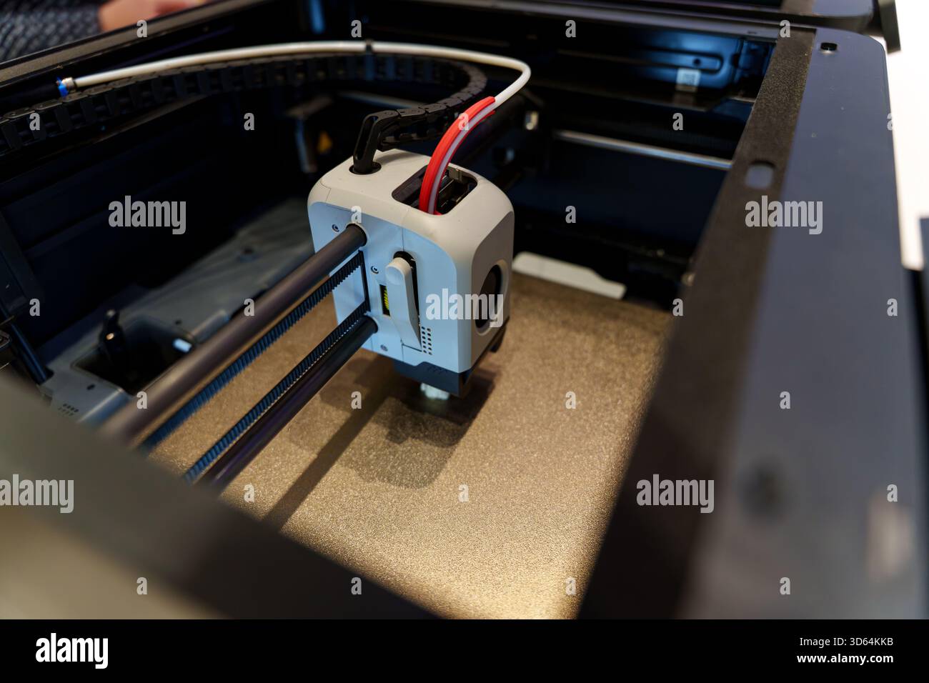 Eine Nahansicht eines 3D-Druckers in Aktion, die den Druckkopf und die Schienen mit angeschlossenen Kabeln im Gehäuse des Geräts zeigt. Hochwertige Fotos Stockfoto