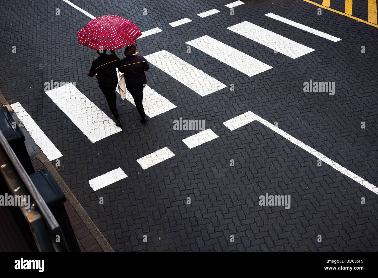 Leute, die mit dem roten Regenschirm über die Fußgängerüberquerung laufen Stockfoto