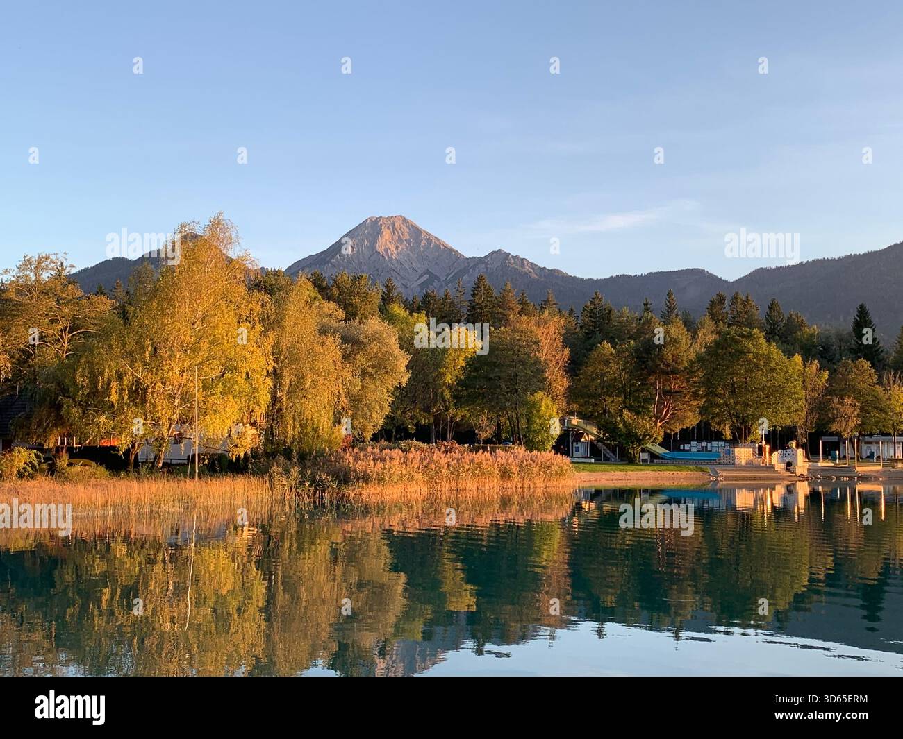 Berglandschaft mit goldenen Bäumen, die sich während des Sonnenuntergangs im frühen Herbst in einem ruhigen See spiegeln - Smartphone-aufgenommenes Stockfoto