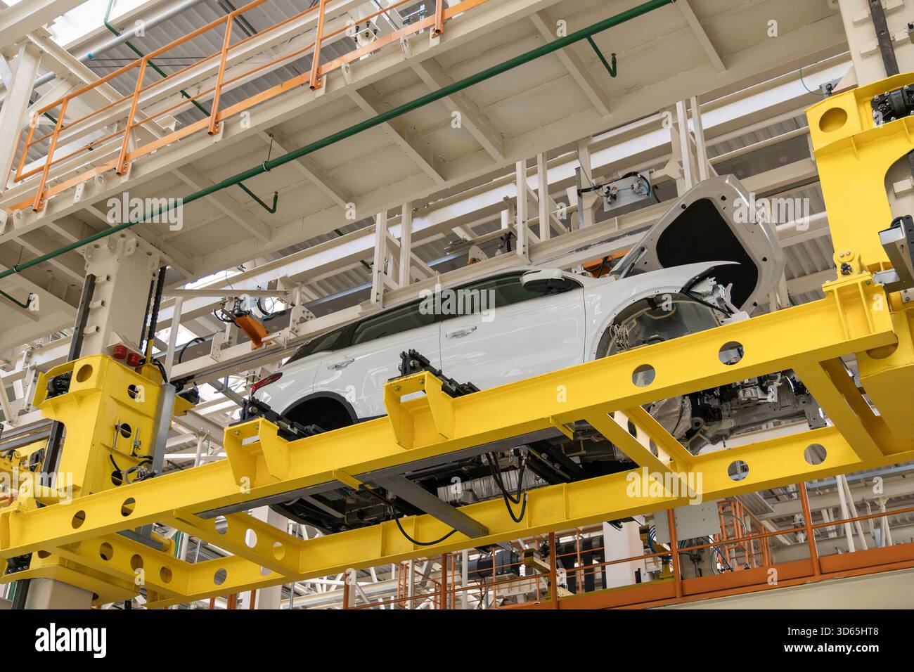 Eine moderne, automatisierte Produktionslinie in einer Montagehalle, die mit einer neuen weißen Karosserie ausgestattet ist, die auf einem gelben Fördersystem aufgehängt ist Stockfoto