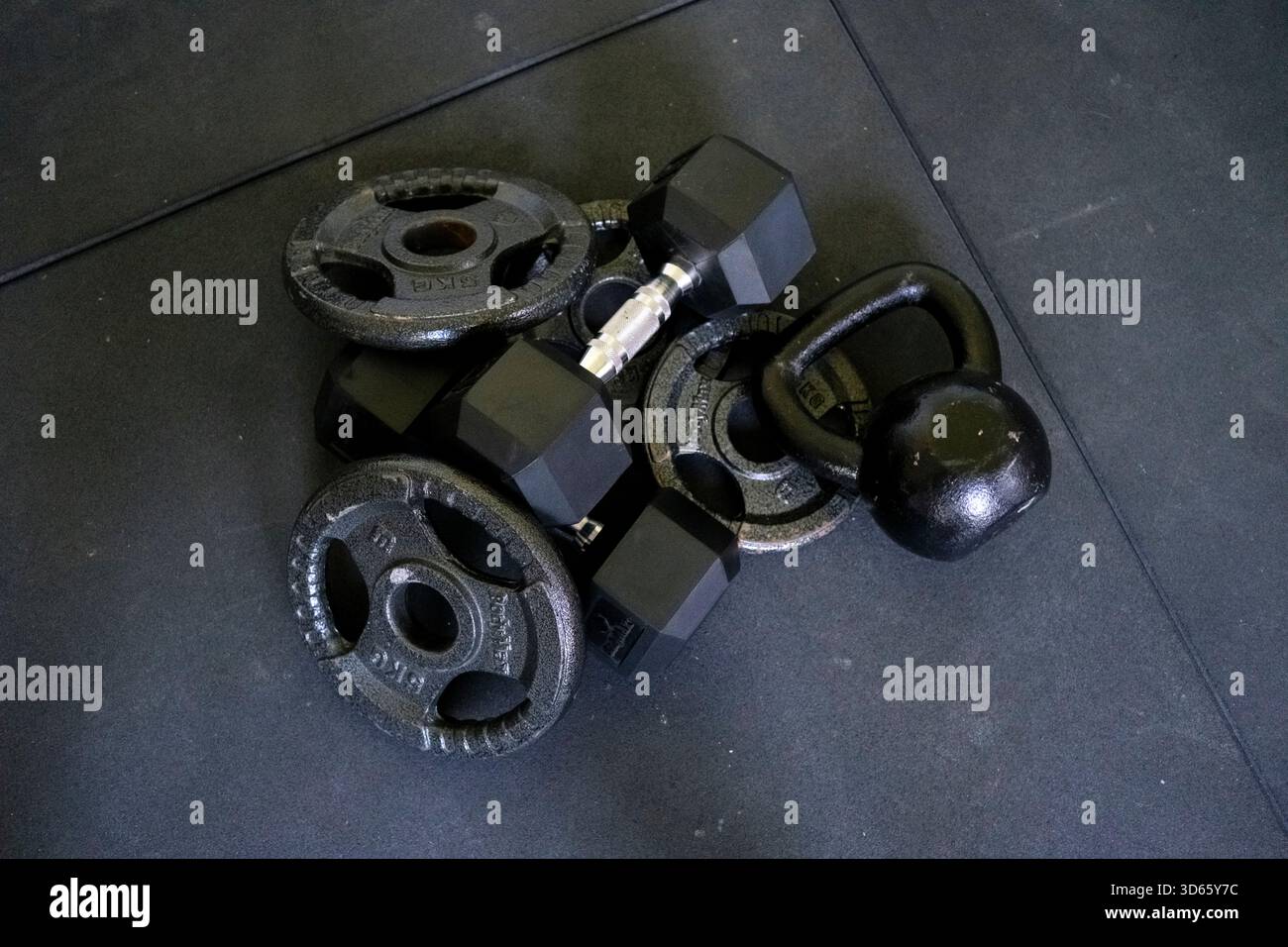 Eine Sammlung verschiedener Gewichte und Kurzhanteln liegt auf dem Boden des Fitnessstudios und betont einen dynamischen Trainingsbereich, der für intensive Trainingseinheiten und Pers geeignet ist Stockfoto