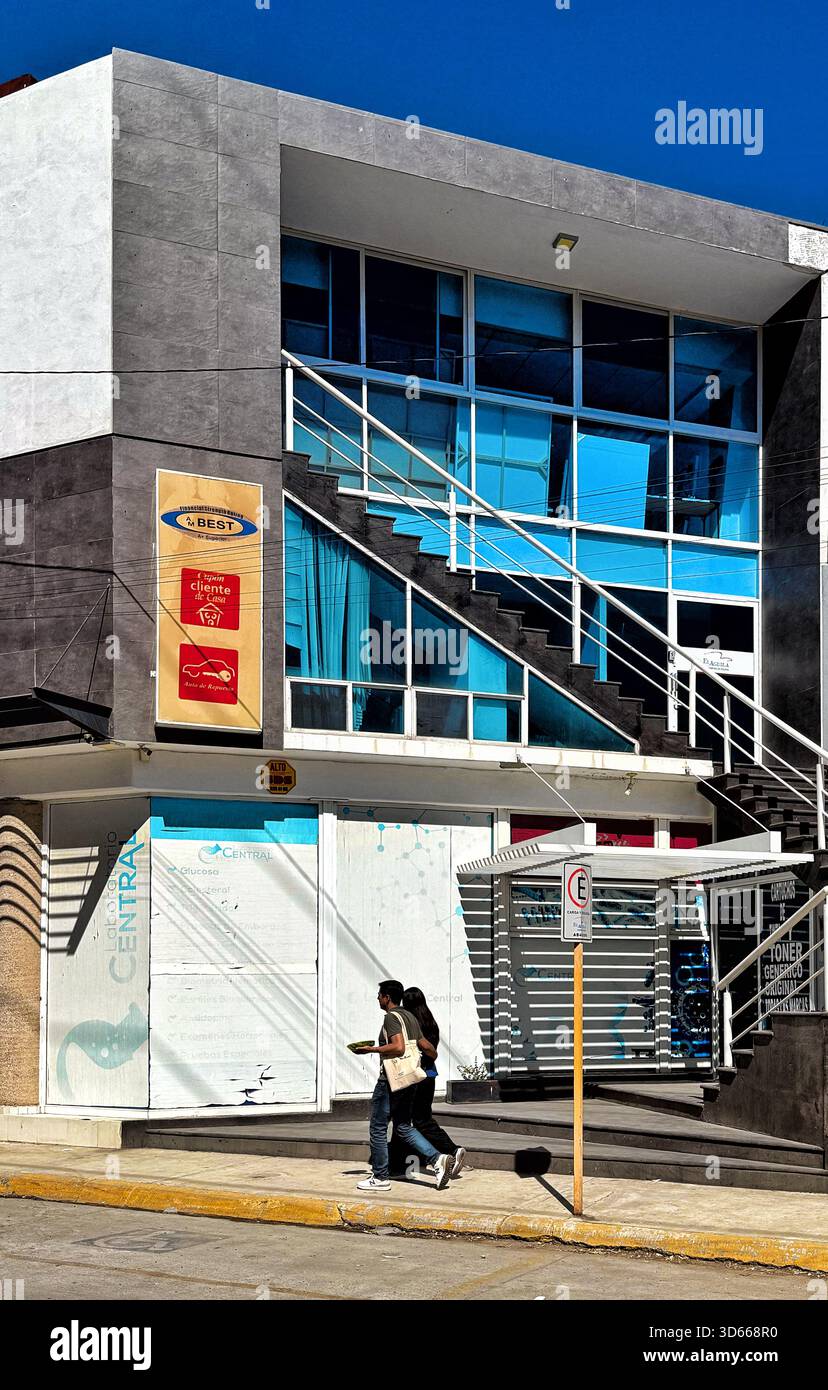 Modernes Geschäftsgebäude mit Glasfassade und Außentreppe an sonnigen Tagen mit zwei Personen auf dem Gehweg - Smartphone-aufgenommenes Stockfoto
