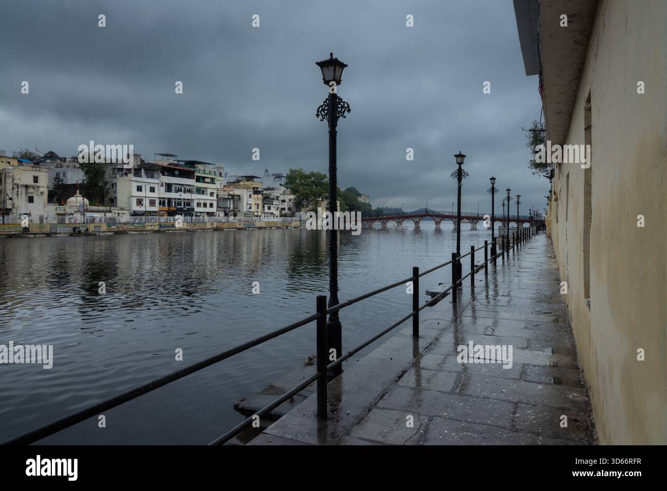 Nasser Fußweg am See mit Laternenpfosten entlang des Ufers des Pichola-Sees in Udaipur an einem bewölkten Monsuntag. Stockfoto
