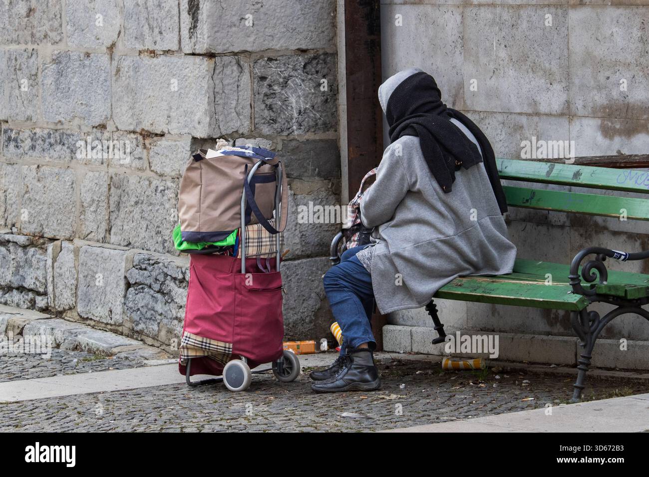 Ljubljana, Slowenien 19. Oktober 2025 Frau, die auf einer Bank mit Karren in der Nähe einer Steinmauer sitzt Stockfoto