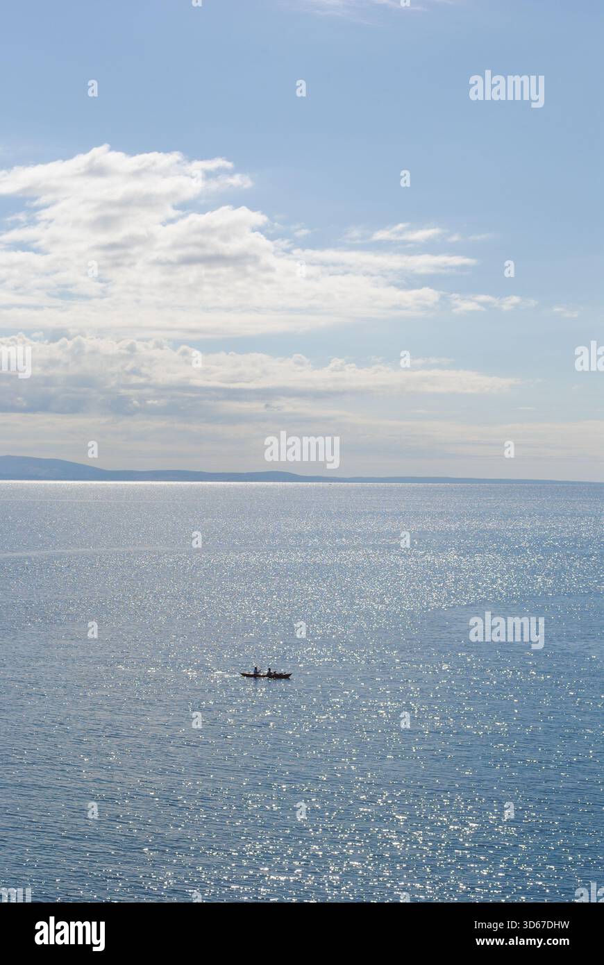 Zwei Personen in einem Kajak, die wie Punkte in der Ferne auf dem großen, blau glänzenden Meer unter dem wunderschönen mediterranen Himmel aussehen Stockfoto