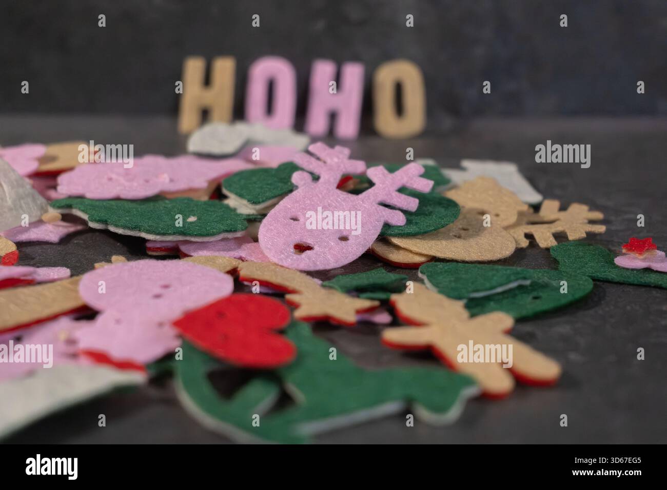 Farbenfrohe Filzdekorationen sind auf einer dunklen Oberfläche verteilt und mit Weihnachtsmotiven wie Rentieren und Blumen versehen, die eine fröhliche und kreative Atmosphäre schaffen Stockfoto